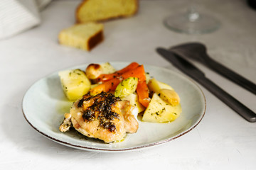 Homemade herb and spice chicken thighs baked with vegetables on a plate on grey background. Homemade lunch. Selective focus