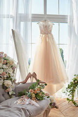 Beautiful beige women's shoes and bridal bouquet on chesterfield sofa with wedding dress in blur...