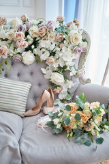 Lush bridal bouquet of roses, freesia, brunia and eucalyptus with satin ribbons and beige bride shoes on high heels on chesterfield sofa, copy space. Wedding morning preparations