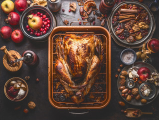 Whole roasted stuffed turkey in baking tray to Thanksgiving dinner on kitchen table with various autumn seasonal ingredients: apples, cranberries, various nuts, chestnuts, spices and flavor , top view