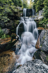 Fototapeta na wymiar Waterfall photograph. Long exposure photo of a beautiful waterfall of Jedlova, Jizerske mountains, Czechia. Motion blurr water in a mountain creek in a deep forest. Alaska like stream with a rocks.