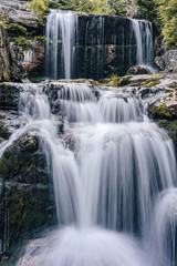 Fototapeta premium Waterfall photograph. Long exposure photo of a beautiful waterfall of Jedlova, Jizerske mountains, Czechia. Motion blurr water in a mountain creek in a deep forest. Alaska like stream with a rocks.