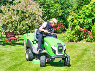 Mature woman driving a tractor lawn mower in garden with flowers