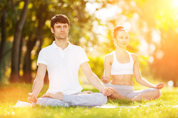 Couples Yoga, man and woman doing yoga exercises, meditate in the sunny park. Yoga outdoor. Concept...