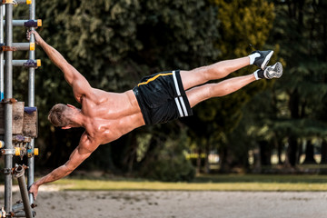 Fit Muscular man performing calisthenics fitness  workout on outdoor scaffolding