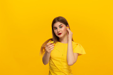 Happy young model in a yellow tee listens to music with wired headphones standing over yellow background