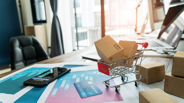 E-commerce. Paper boxes in shopping cart and credit card with smartphone on sales data economic growth graph, online shopping and payments, banking, buying and selling services online on network.