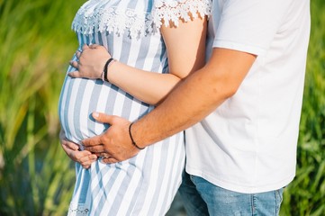 Image of pregnant couple. Husband touching his wife belly with hands. Pregnant woman outdoors