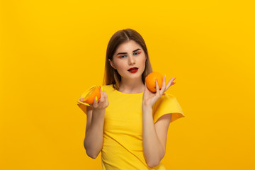 Young model in a yellow tee holds oranges standing over yellow background.