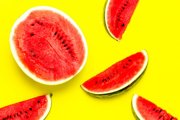 Half and pieces of ripe juicy red watermelon on bright yellow background. Flat lay, top view, copy space. Creative summer food concept