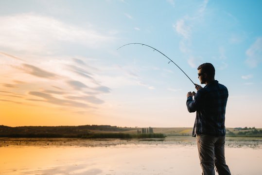 Fisher man fishing with spinning rod on a river bank at misty foggy sunrise. fisher with spinning. spinning concept