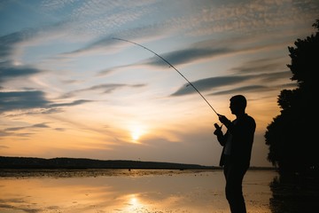 Fisherman at sunset on the river .Beautiful summer landscape with sunset on the river. Fishing. spinning at sunset. Silhouette of a fisherman