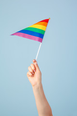 Closeup of a hand waving a small rainbow flag against a light blue background