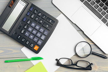 Angled View of laptop Computer Keyboard and glasses with Various Office Supplies on wooden Desk