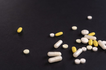 Tablets and pills scattered on a black background. Treatment of illness, malaise. Pharmacology