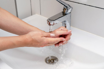 Women washing hands in the bathroom in the sink using purple color soap. Female hands under the tap and the water jet