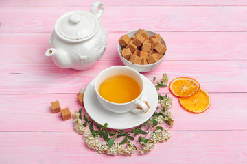 Cup of tea with sugar cubes and flower branches on wooden table close up