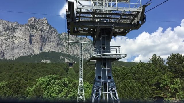 Cableway on picturesque mountains. Tracking shot on moving cableway above forest to steep rocky wall at summer. Cabin driving over huge green trees. Amazing nature landscape. First person video.
