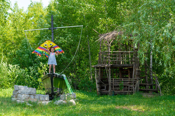Fototapeta na wymiar The little girl holds a bright kite in her hands and smiles against the green forest. A small child 5 years old stands on a boat next to a tree house.