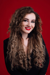 Beauty young woman with curly big and long hair. Glamour lady, beauty girl on red background. Beautiful woman portrait. Wavy hair, perfect make up, red lips, thick eyelashes.