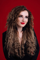 Beauty young woman with curly big and long hair. Glamour lady, beauty girl on red background. Beautiful woman portrait. Wavy hair, perfect make up, red lips, thick eyelashes.