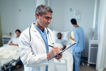 Male doctor writing on clipboard in the ward at hospital