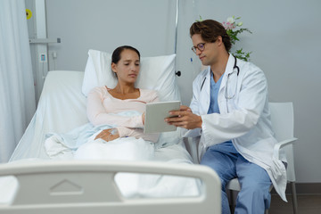 Male doctor and female patient discussing over digital tablet in the ward