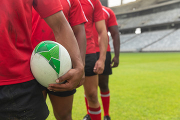 Male rugby players standing together with rugby ball in stadium