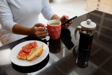 Woman using mobile phone on a dining table at kitchen