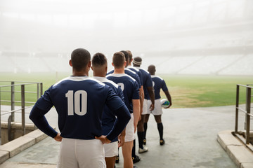 Diverse male rugby players standing at the entrance of stadium in a row for match
