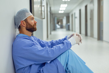 Tensed male surgeon sitting in the corridor