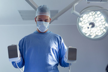 Fototapeta na wymiar Male surgeon holding defibrillator in operation room at the hospital