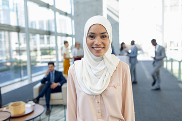 Young pretty businesswoman in hijab looking at camera while standing in modern office.