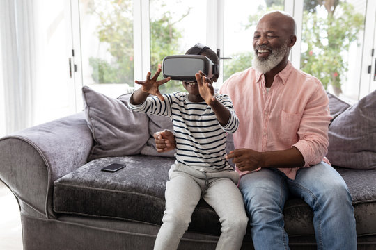 Grandson with grandfather using virtual reality headset in living room - Powered by Adobe
