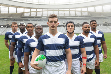 Group of diverse male rugby players standing together with rugby ball in stadium - obrazy, fototapety, plakaty