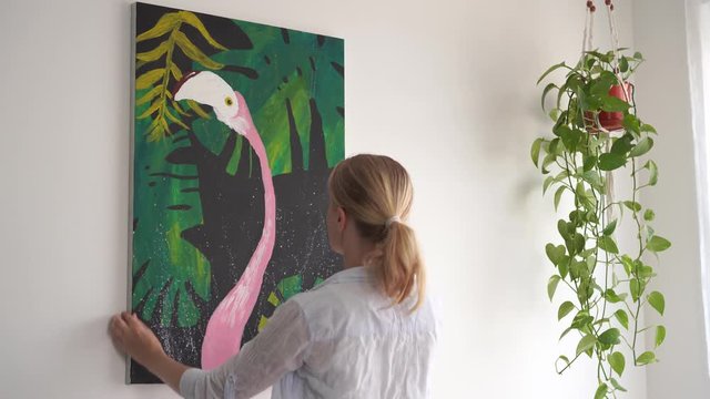 Moving to a new home. A young blonde woman laying down a picture on canvas in a room.