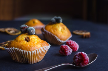 Sweet muffins with berries on dark textured background.
