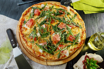Pizza with bacon, cheese and herbs on a wooden dish on a black wooden background
