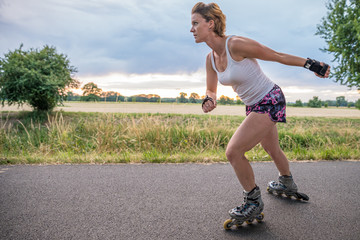 young woman rides on roller skates on an asphalt trail outside the city in summer