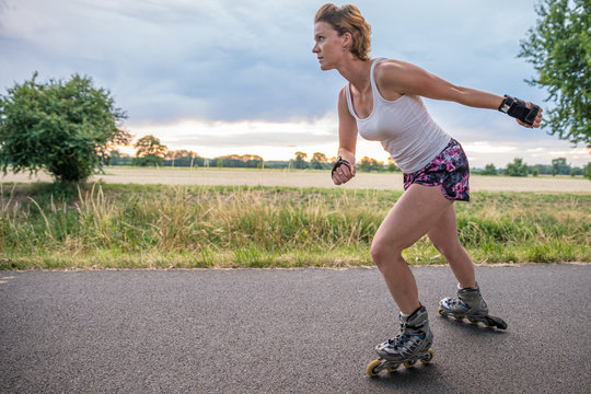 young woman rides on roller skates on an asphalt trail outside the city in summer