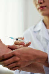 Close-up of female doctor holding a syringe and make an injection into hand of her patient at hospital