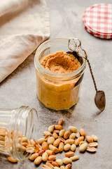 Fresh homemade creamy Peanut Butter in a glass jar on gray background.Kinfolk and comfort food atmosphere concept.