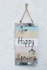 Happy spring written on an wooden board hanged on a wall.