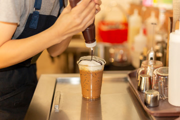 Barista squeezing chocolate cream on cream in iced chocolate drink.