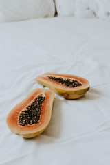 Tropical exotic orange papaya fruit lying on the bed with white sheets and pillows. Summer and travel concept.