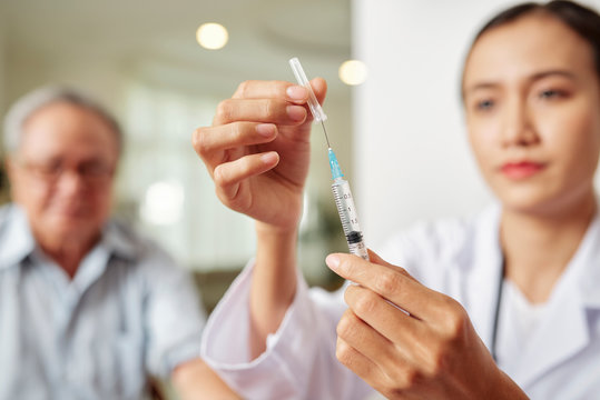 Close-up Of Young Female Doctor Holding Syringe And She Is Going To Make A Vaccination To The Patient In The Background At Hospital