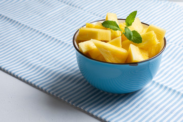 Blue bowl with fresh pineapple on light striped tablecloth - image