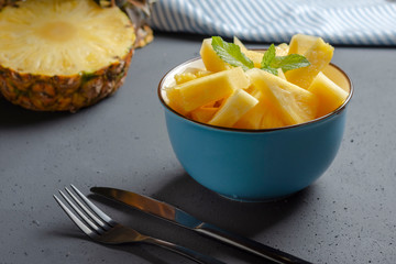 Blue bowl with fresh pineapple on rustic black background with cutlery - image