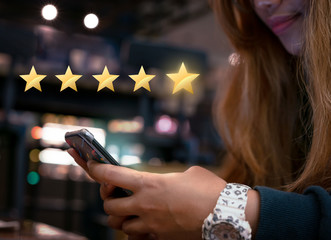 Woman internet shopping on smartphone submitting 5 gold star satisfaction feedback - Millennial...