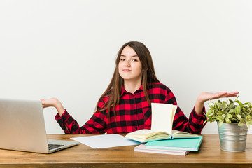 Young teenager going back to her routine doing homeworks doubting and shrugging shoulders in questioning gesture.